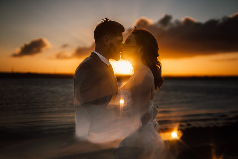 A bride and groom along the Swale estuary at Kent barn wedding venue, The Ferry House, at sunset.