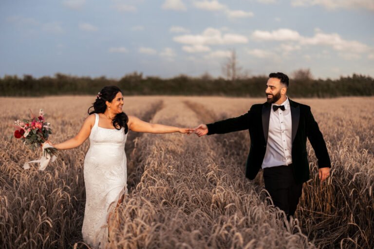 A bride and groom holding hands through fields near The Ferry House wedding venue in Kent.