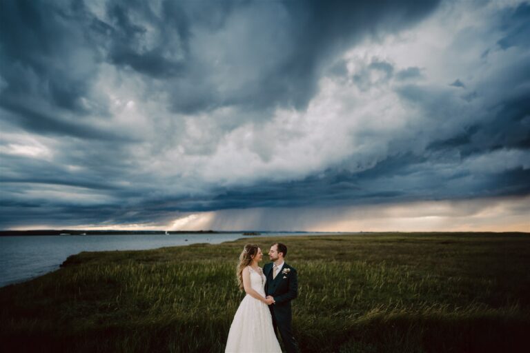 A wedding couple gazing at each other under dramatic skies, beside the Swale estuary in Kent