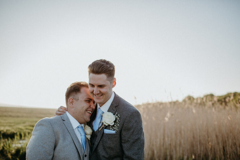 Two grooms by the waterside of the Swale estuary on their wedding day at The Ferry House in Kent.