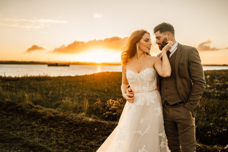 A wedding couple sharing a romantic moment in front of the Swale estuary in Kent at sunset