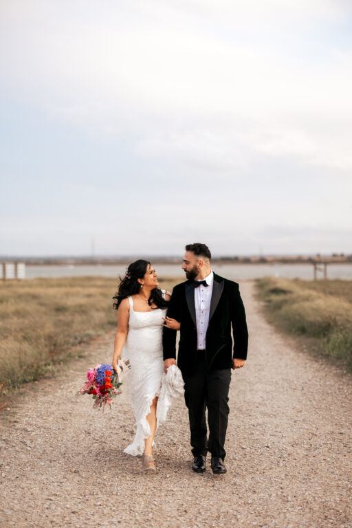 A wedding couple walking arm in arm away from the Swale estuary at Kent barn wedding venue, The Ferry House.