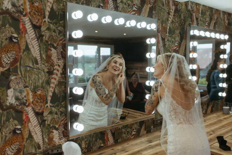 A bride adding the finish touches in front of a mirror in the Garden Lodge at Kent wedding venue, The Ferry House.