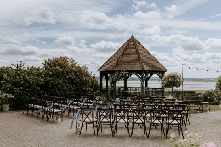 An outdoor ceremony set up at The Ferry House wedding venue in Kent, with the Swale estuary in the background.