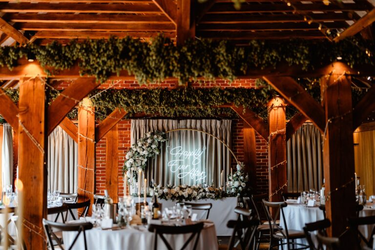 The Hop Barn at Kent wedding venue The Ferry House set up for a wedding breakfast, with a sweetheart table and neon sign.