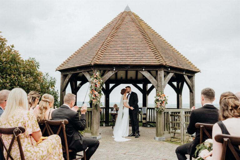 A bride and groom during their wedding ceremony under the Oak Gazebo at waterside wedding venue The Ferry House in Kent.