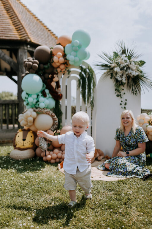 A little boy in front of a beautiful balloon arch and flower display at a Christening.