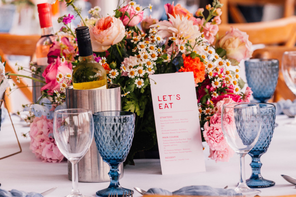 A bold table setting at The Ferry House barn wedding venue in Kent with blue glasses and vibrant florals.