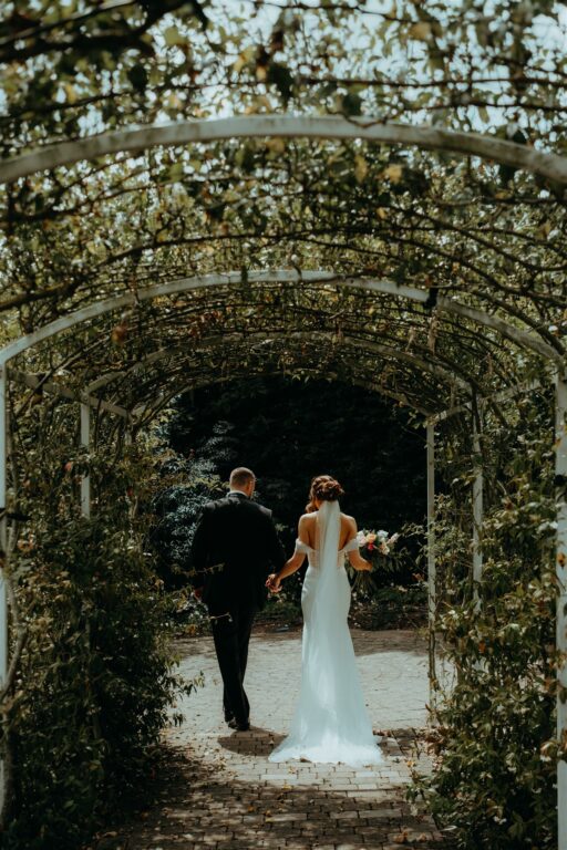 A couple at The Ferry House Best Event Venue in Kent walking through the rose arch.