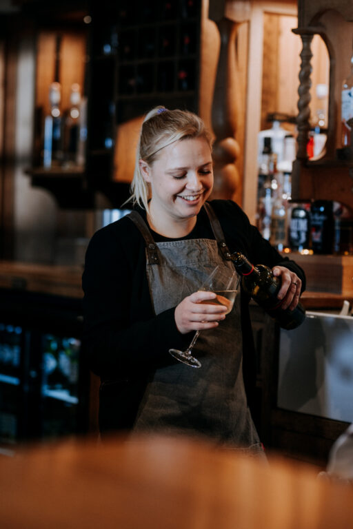 Smiling front of house staff pouring a drink